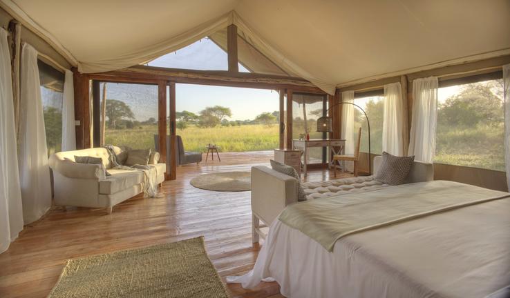 Luxury tented suite interior with double bed and patio overlooking African bush