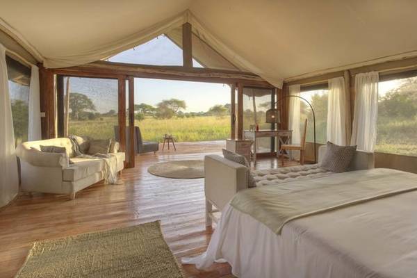 Luxury tented suite interior with double bed and patio overlooking African bush
