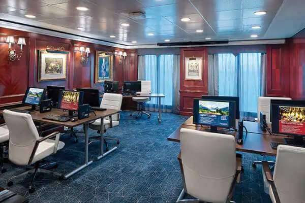 A picture of a room in the Oceania Insignia with computers, seats and blinds with a lovely crimson wallpaper