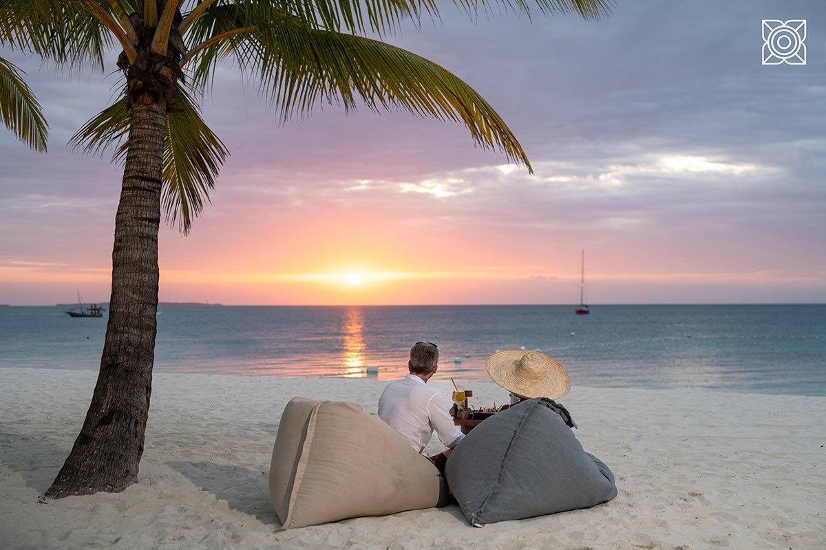 Two people sitting on bean bags on the beach watching the sunset