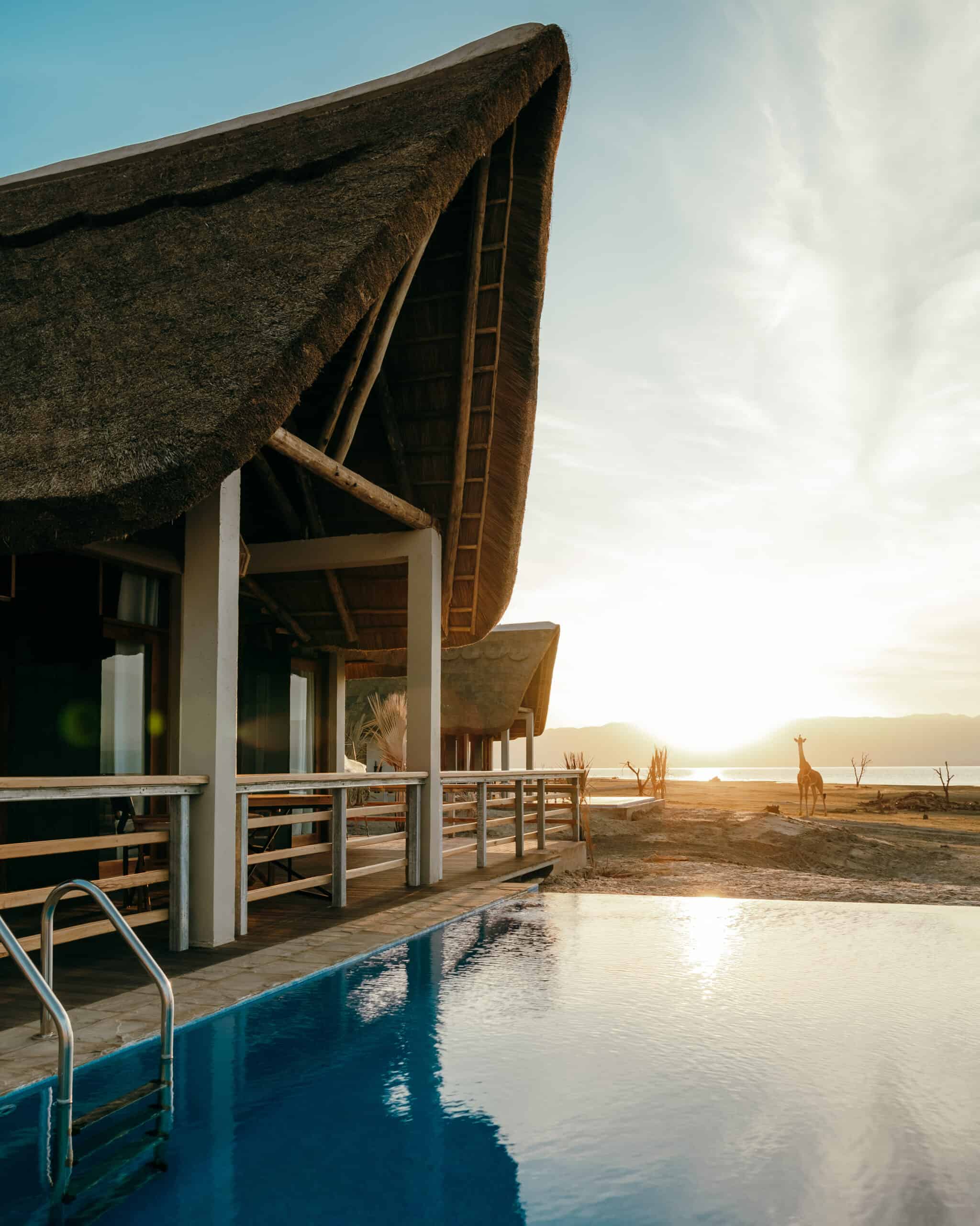 Pool next to thatched chalet with sunsetting