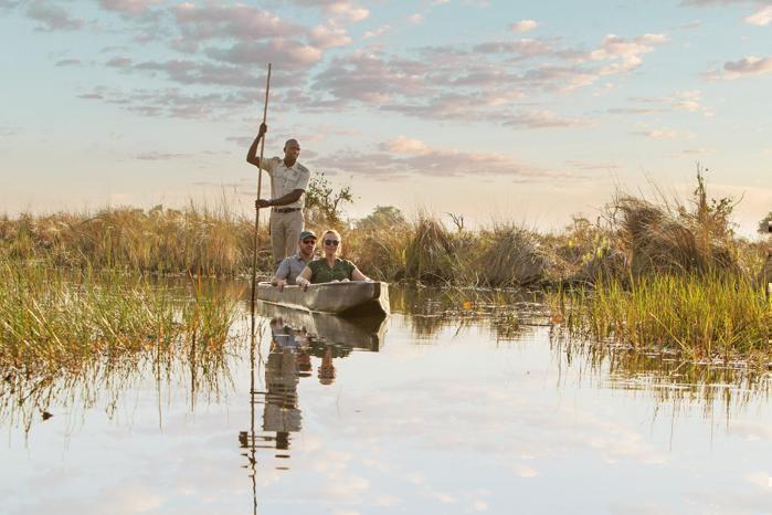 Mokoro with two people seated and one person guiding through the delta