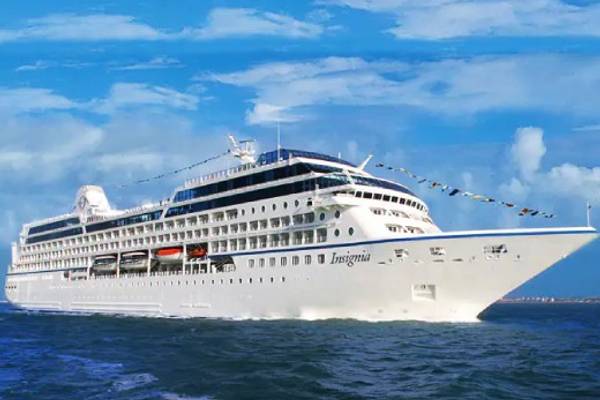 Oceania Insignia cruise ship sailing on a deep blue sea with turquoise sky and clouds in the background.