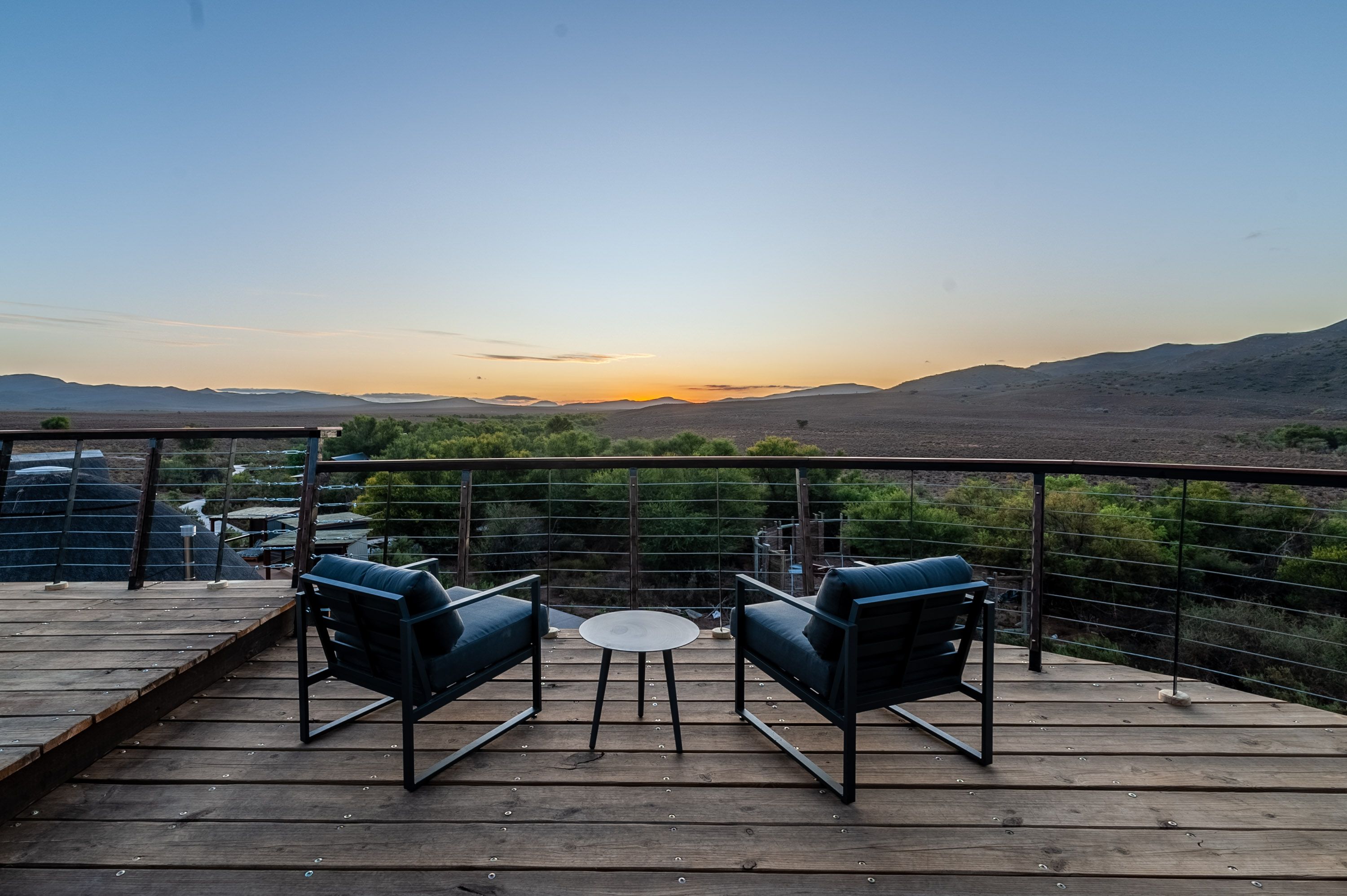 A tranquil viewing deck with to chairs looking out over the lands at sun set