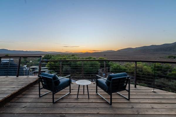 A tranquil viewing deck with to chairs looking out over the lands at sun set