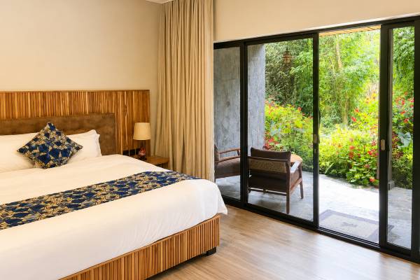 King size bed in room with veranda overlooking green garden