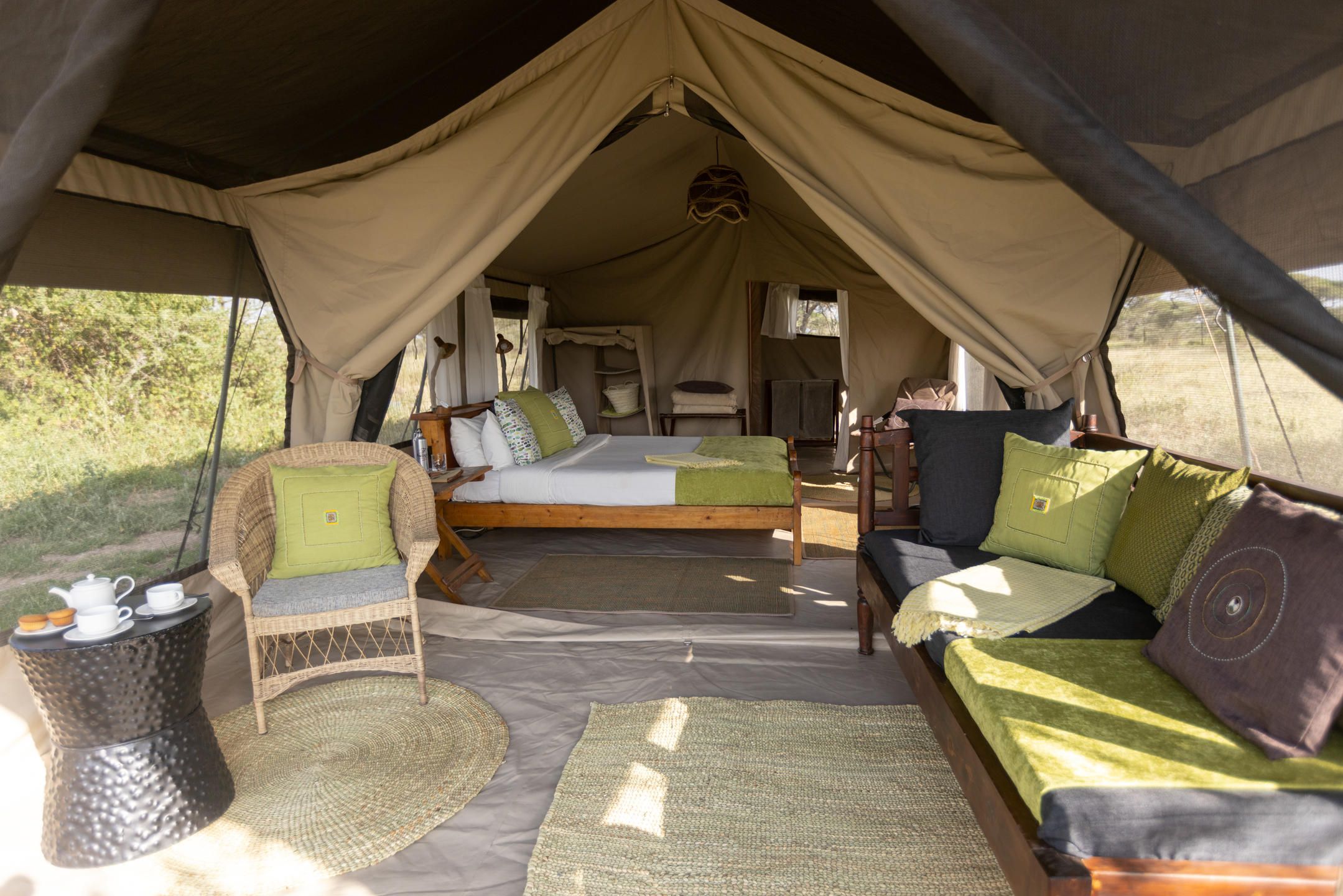 Interior of spacious canvas tent with lounge area and double bed bedroom