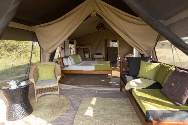 Interior of spacious canvas tent with lounge area and double bed bedroom