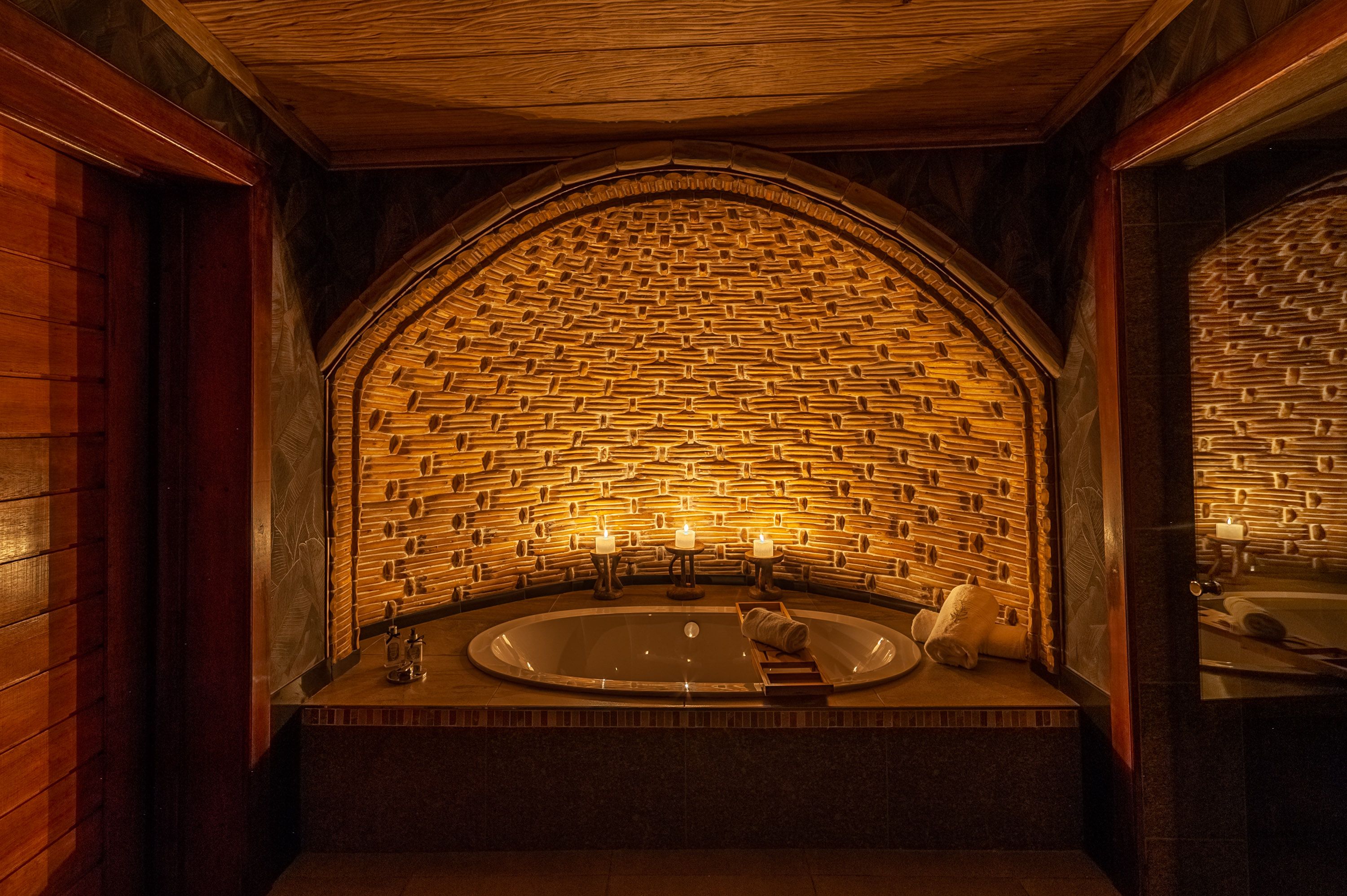 A candlelit bath tub with a mosaic tiled wallbehind it