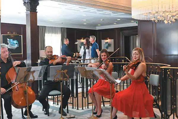 A picture of the entertainment room aboard the Oceania Insignia with people playing the chello and the violin.