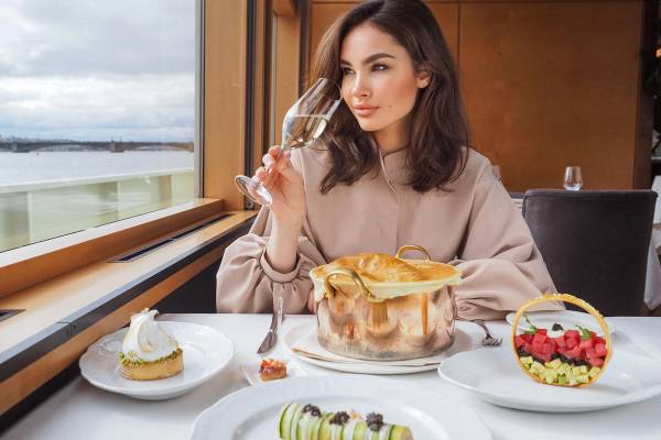 An elegant woman enjoys fine dining on a luxury cruise ship with a glass of champagne and some delicious plates of food.