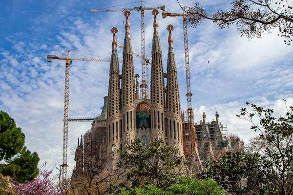 The Basilica de la Sagrada Familia with cranes building it while the sky brightens everything up in the background.
