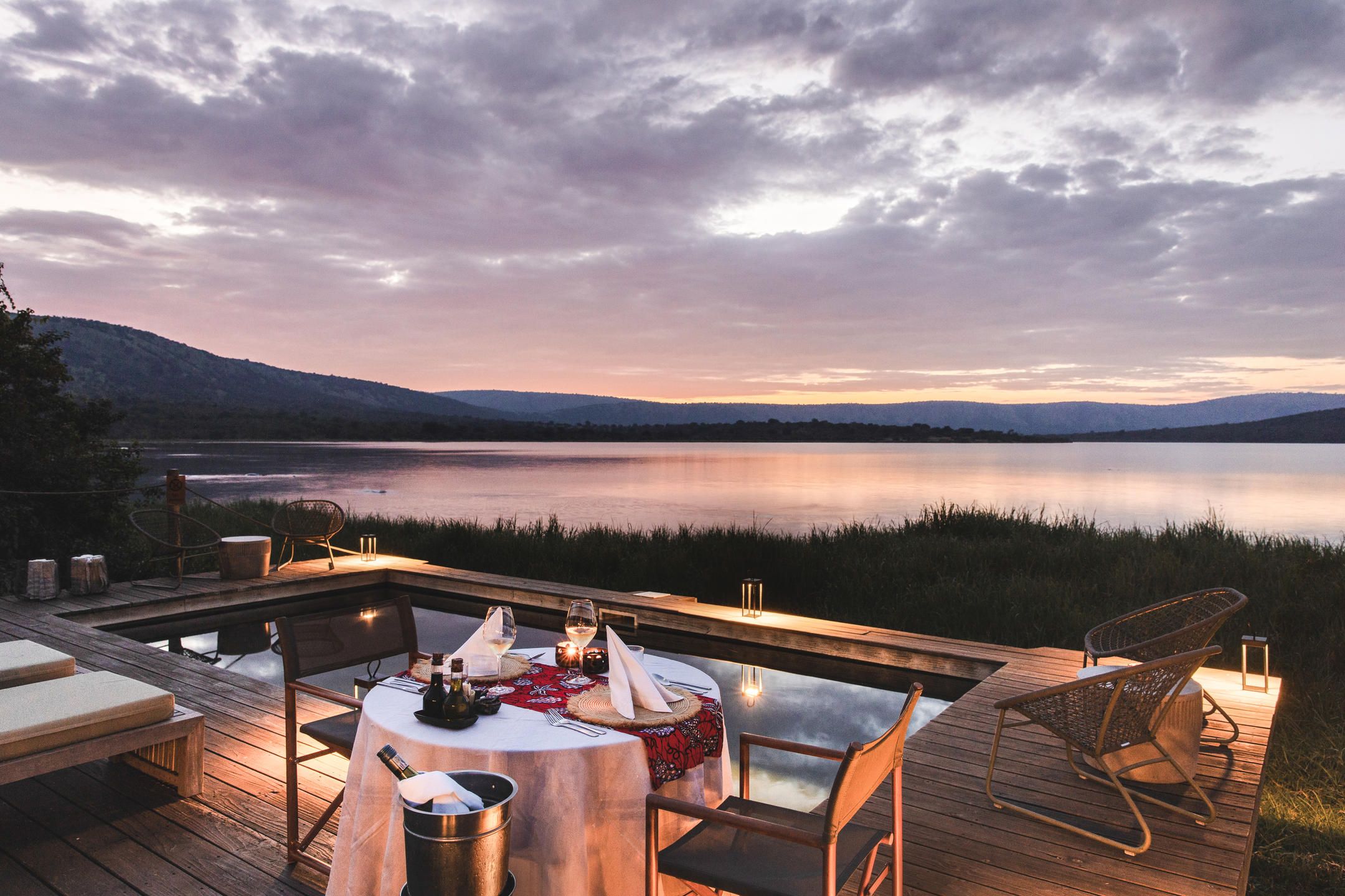 Dinner table set on a balcony overlooking a pool and Lake Rwanyakazinga