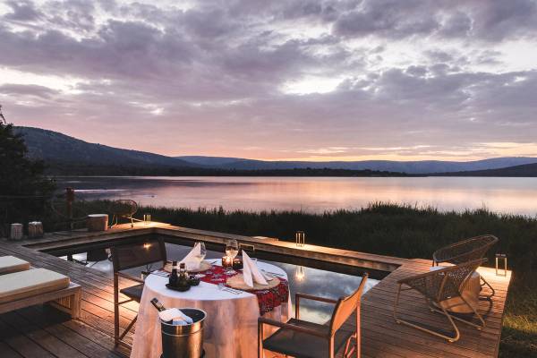 Dinner table set on a balcony overlooking a pool and Lake Rwanyakazinga
