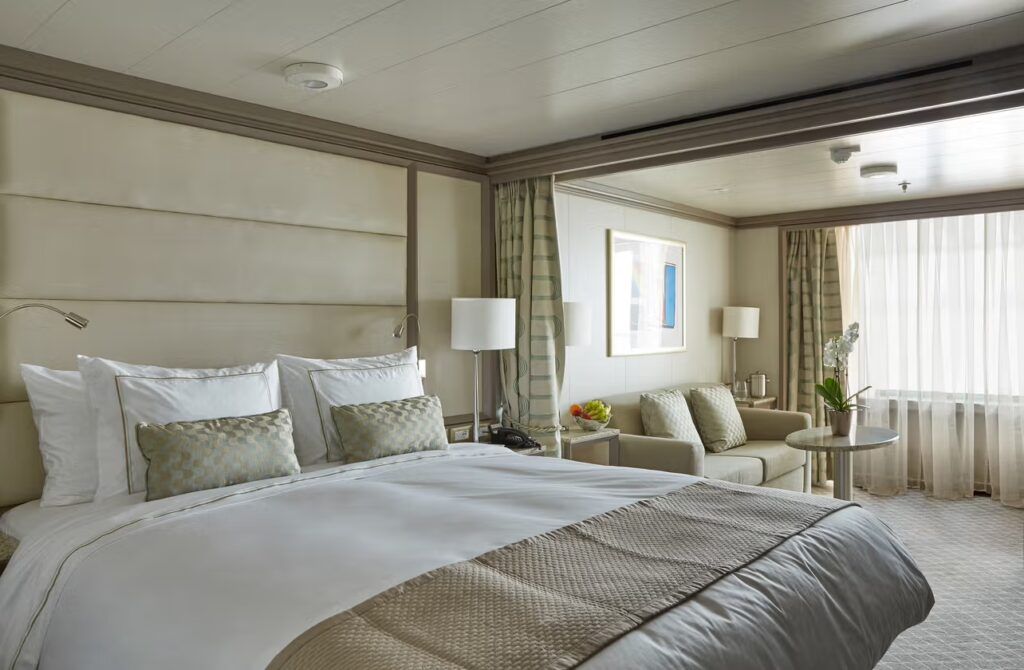 An elegant double cabin on the Silver Muse Cruise ship ith white linens and beige and gold soft trimmings