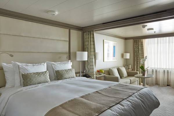 An elegant double cabin on the Silver Muse Cruise ship ith white linens and beige and gold soft trimmings