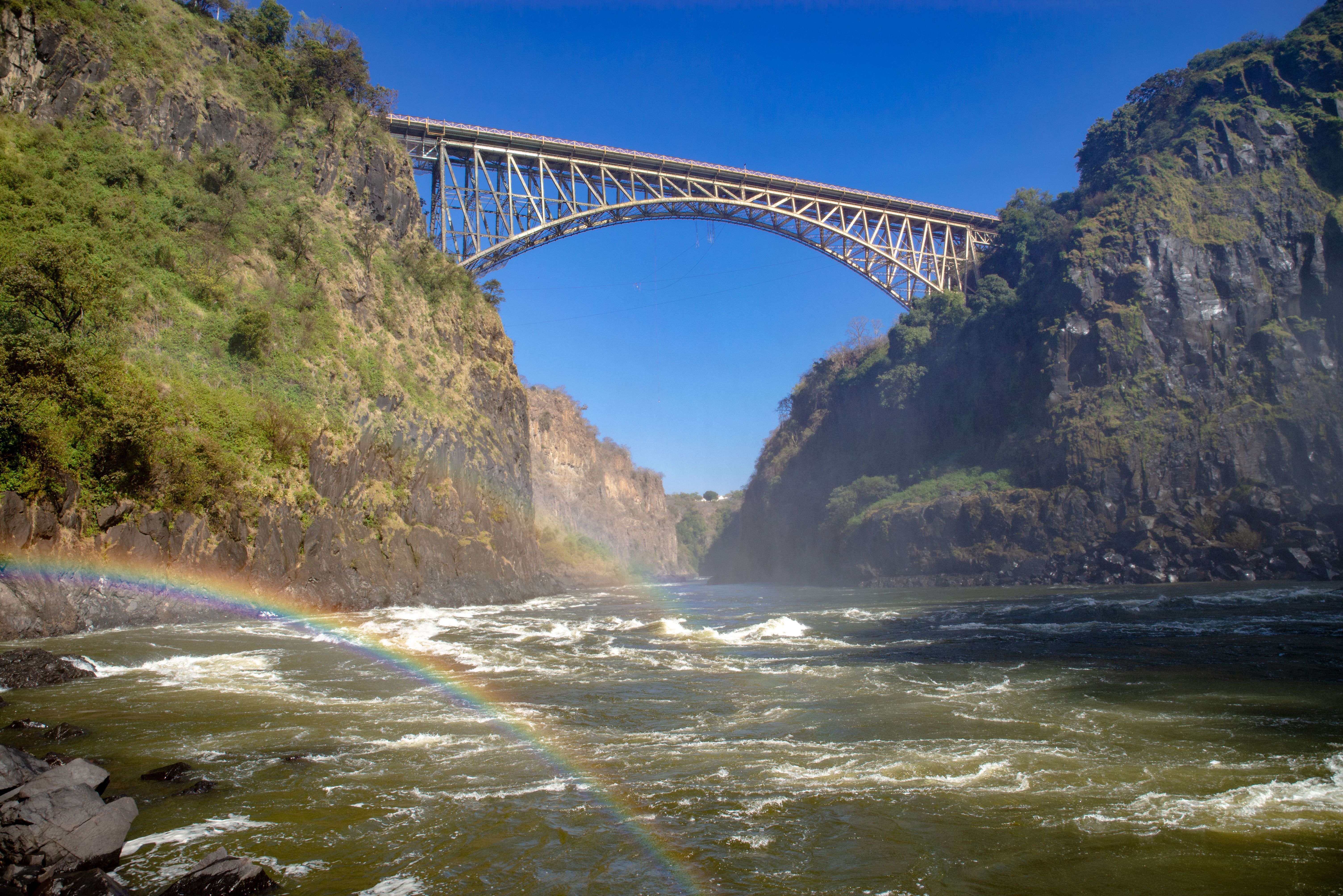 Stunning view of Victoria Falls Bridge surrounded by cliffs and a vibrant rainbow.