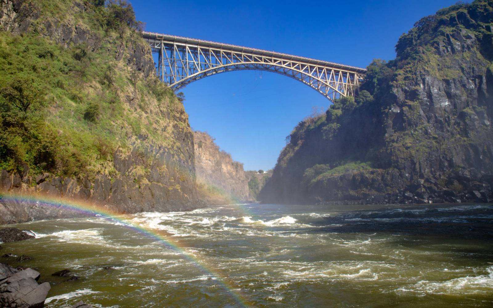 Stunning view of Victoria Falls Bridge surrounded by cliffs and a vibrant rainbow.