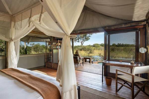 Sable Alley tented suite with wood finishes and person sitting on the terrace overlooking lush African plain
