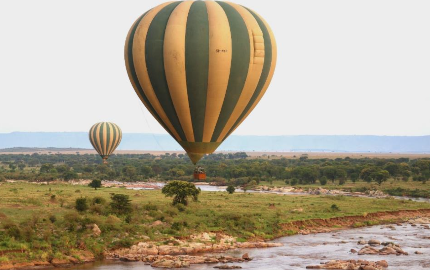 Two hot air balloons floating over river and grassland of Serengeti