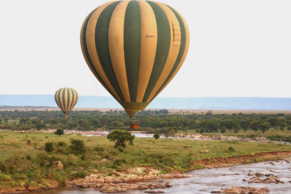 Two hot air balloons floating over river and grassland of Serengeti