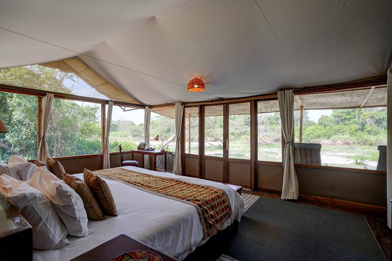 Wooden frame style tent bedroom with double bed and wrap around windows overlooking green surroundings