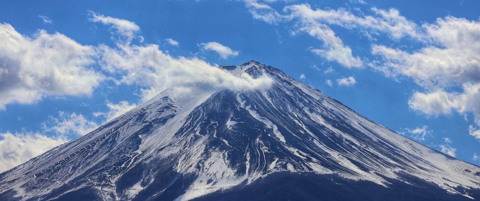 Striking photo of Mount Fuji with snow and clouds against a blue sky, showcasing natural beauty