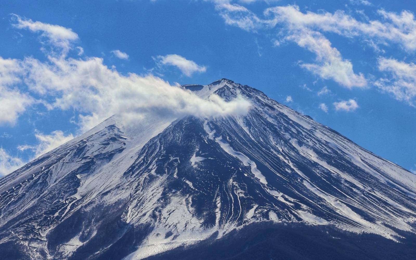 Striking photo of Mount Fuji with snow and clouds against a blue sky, showcasing natural beauty