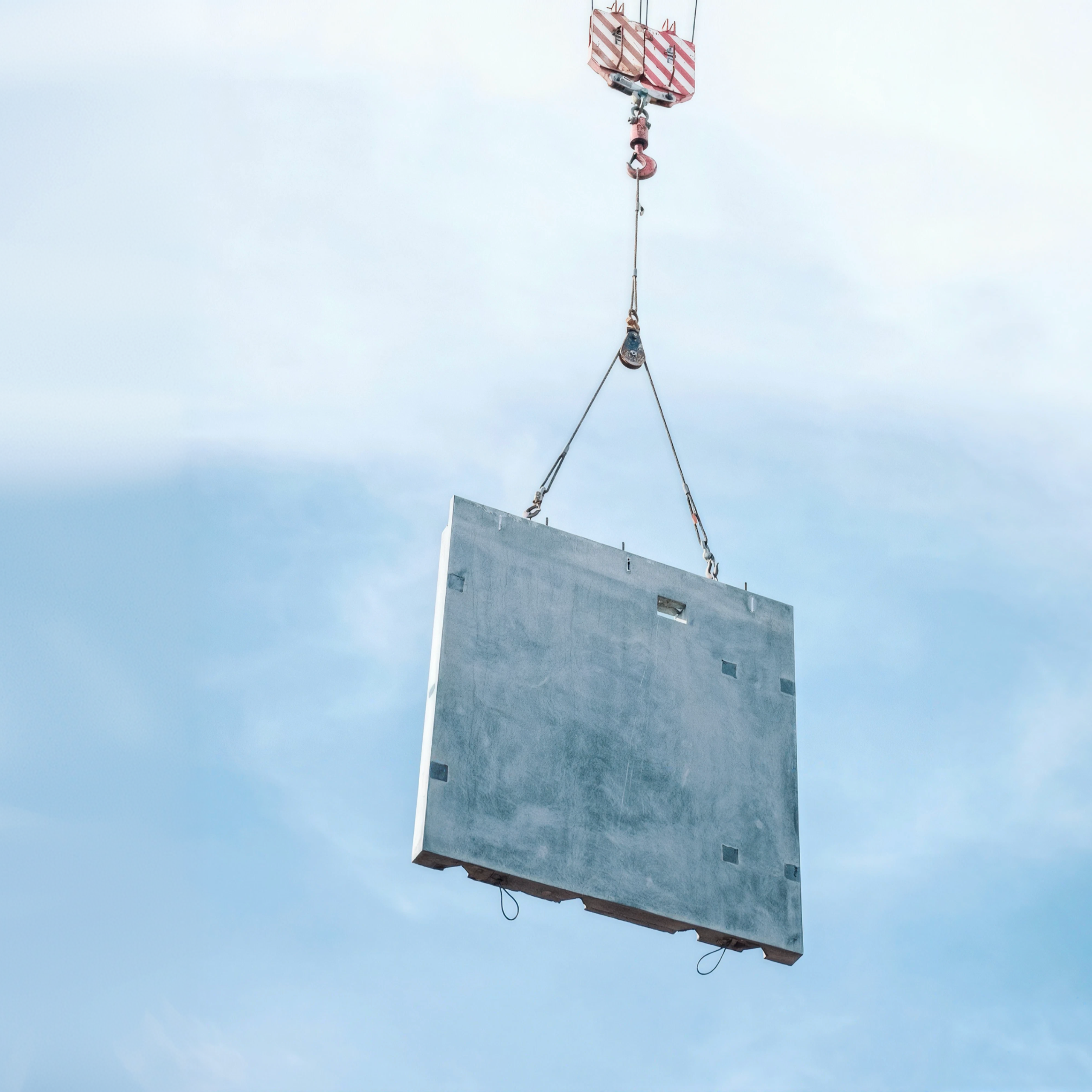 Precast concrete panel suspended from a crane against a blue sky