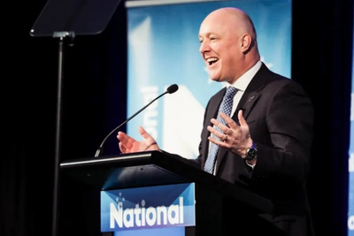 Christopher Luxon laughing and gesturing at a National Party podium