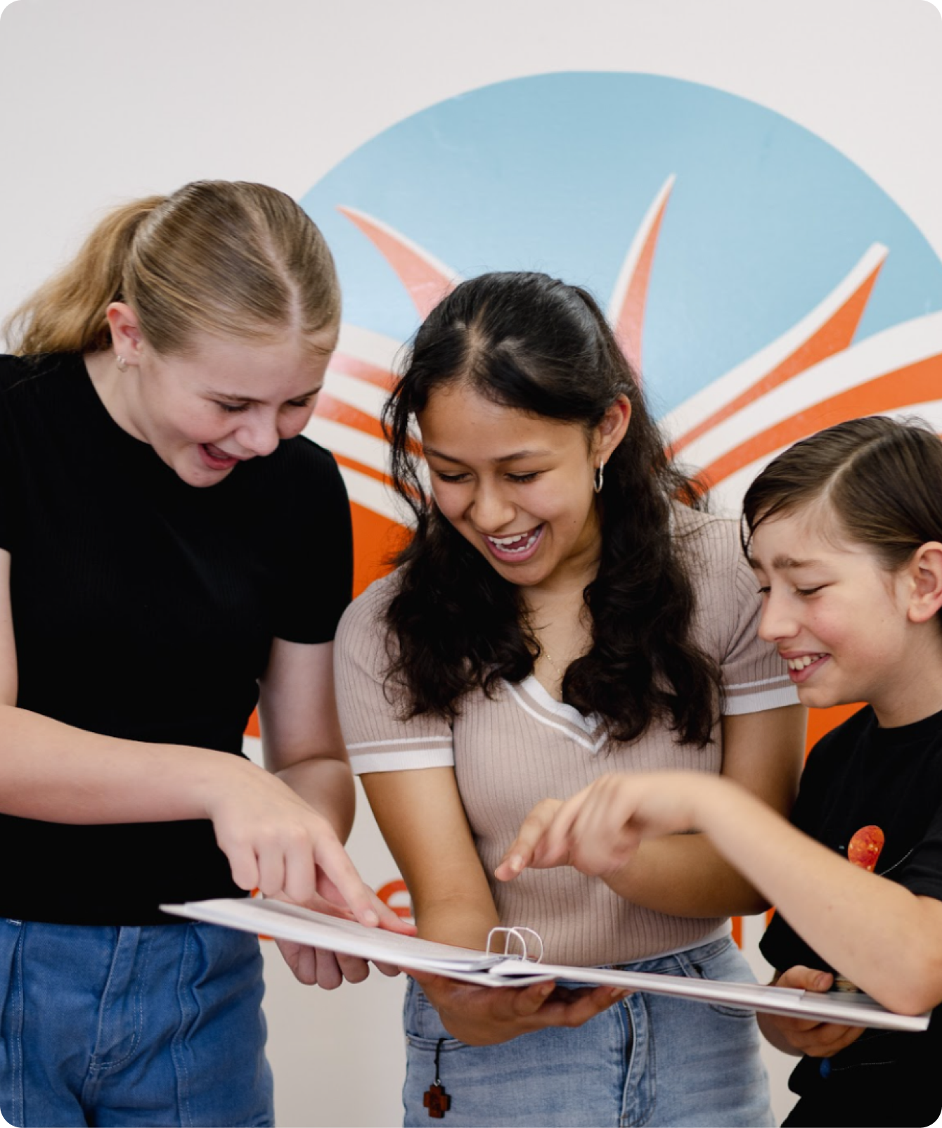 Three students laughing together while reviewing a workbook