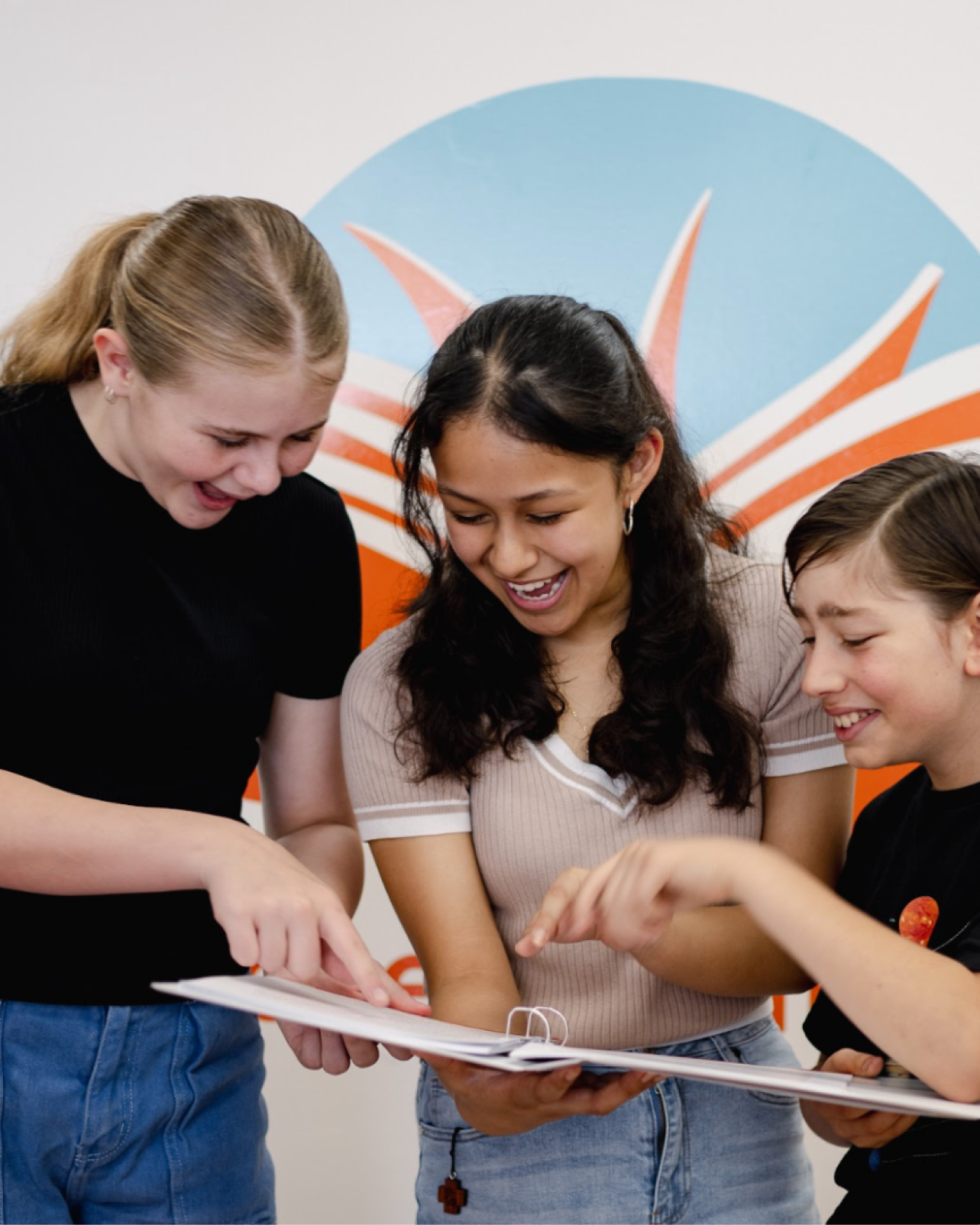 Three students laughing together while reviewing a workbook