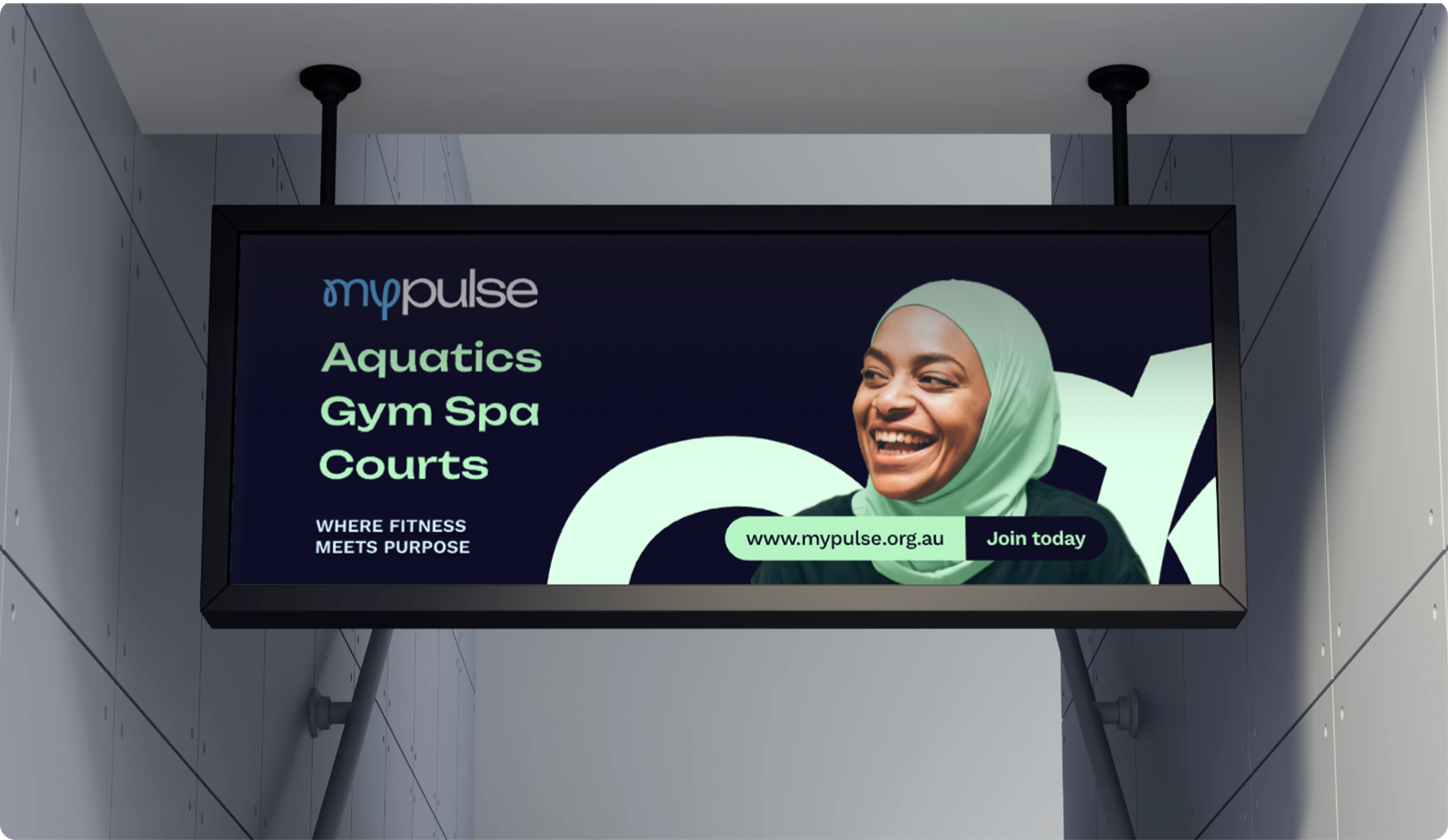 Hanging MyPulse in-centre sign listing aquatics, gym, spa and courts beside a smiling woman in a hijab