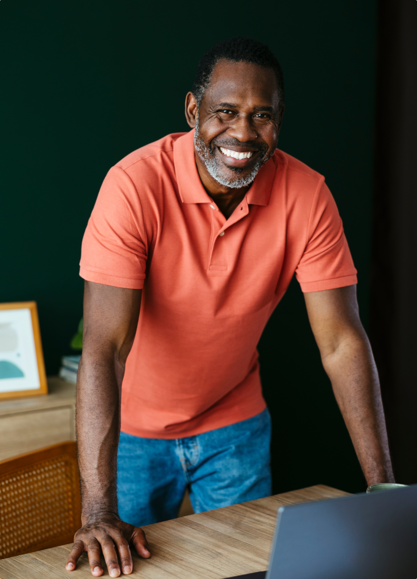 Smiling man in an orange polo shirt leaning on a desk