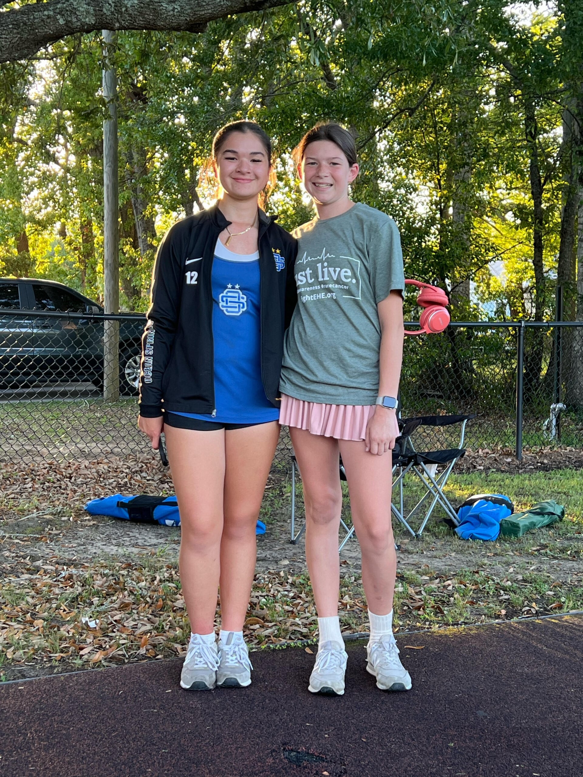 Two young people stand together in front of trees