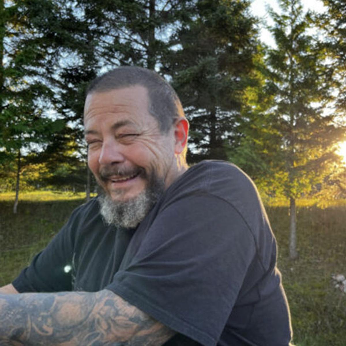 Norm laughs while sitting in an outdoor area.