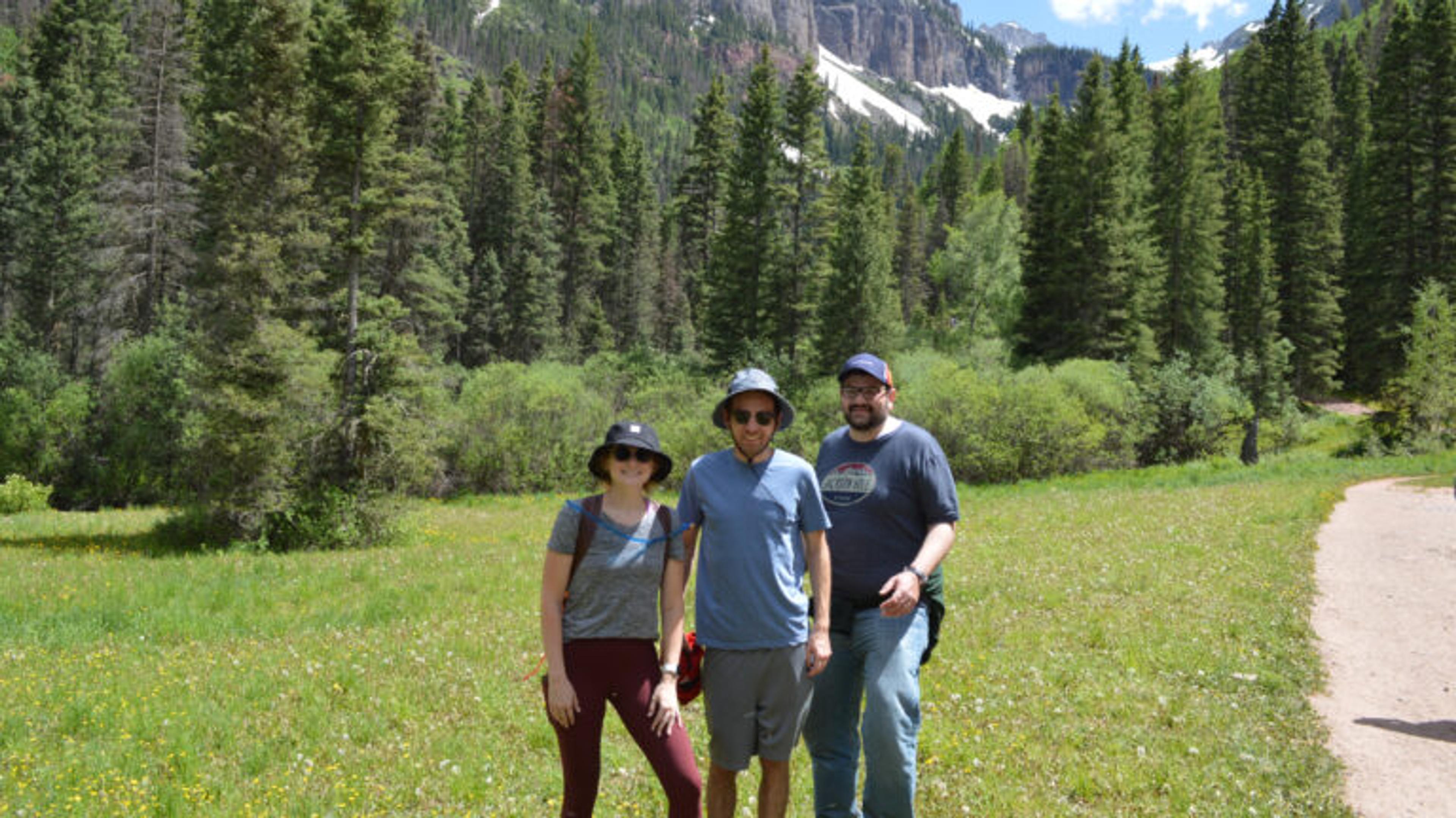 Thre people take a picture together just off a trail on the mountains.