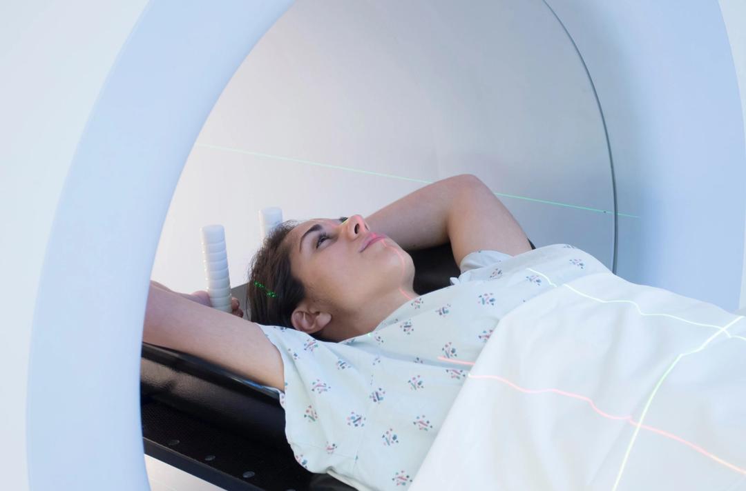 A woman enters an MRI machine with her arms above her head.