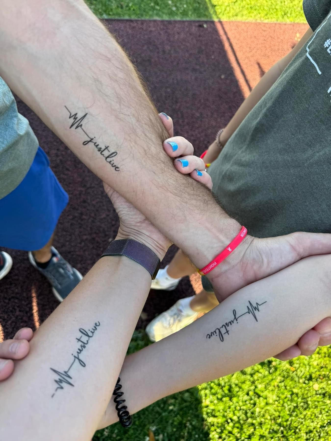 Three people showing of their matching tattoos that read "Just live"