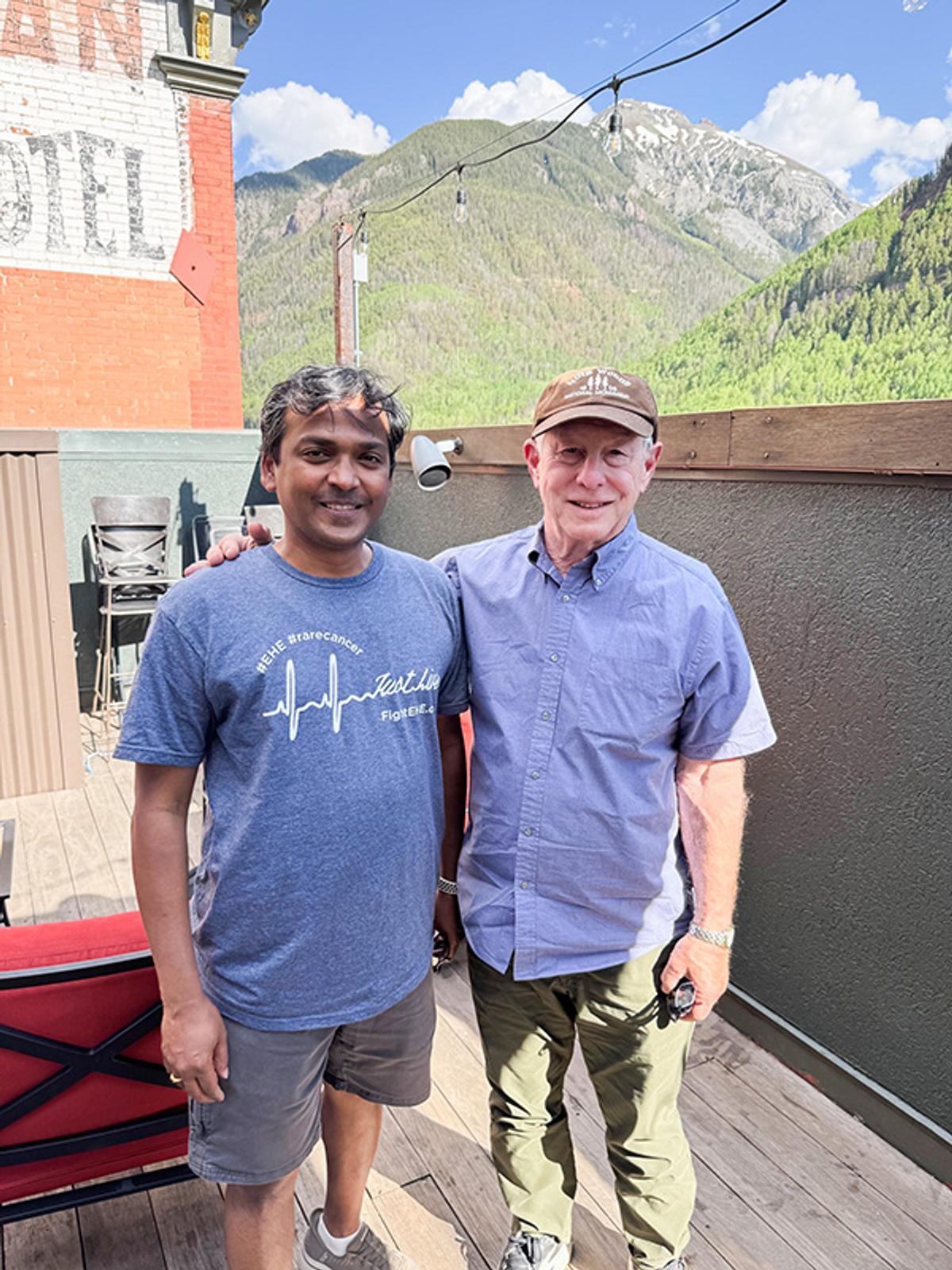 Two gentlemen take a photo together in front of a scenic mountain view
