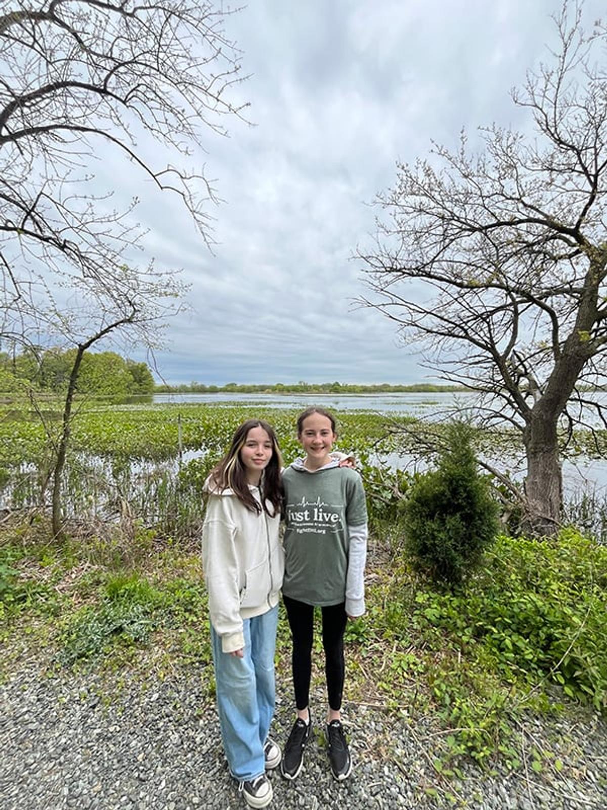 Two friends take a photo along the trail in front of a body of water.