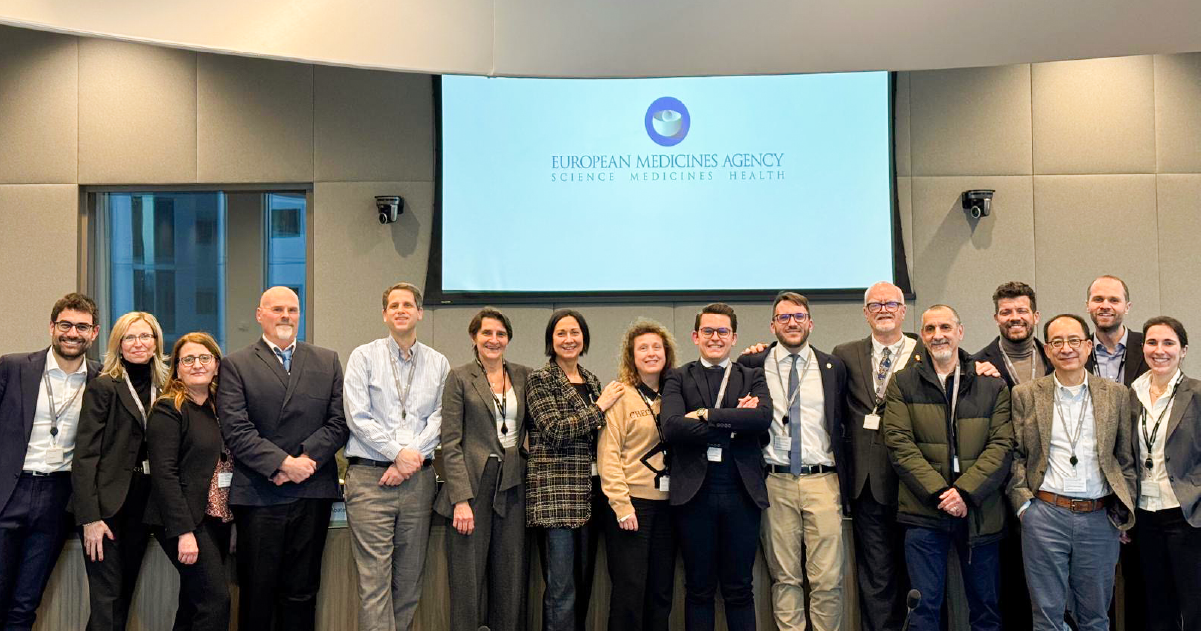 A group of Doctors and researchers come together for a photo in front of a presentation screen.