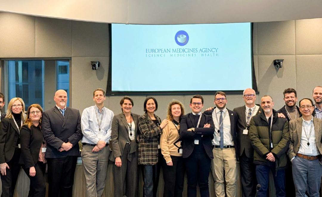 A group of Doctors and researchers come together for a photo in front of a presentation screen.