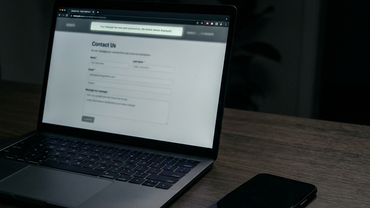 Laptop in a darkened room showing a website contact form that has been submitted, a smartphone lies dark and silent beside it with no notification, communicating the silence after a lead form is submitted with no response