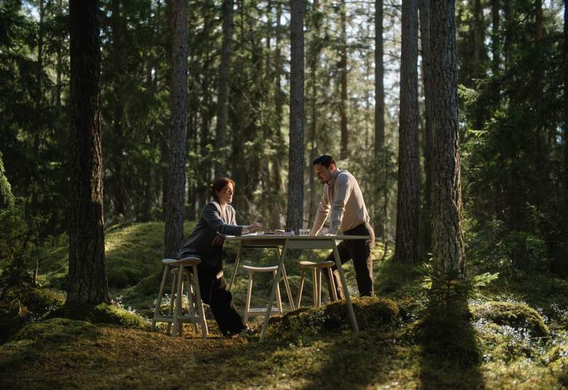 a man and a woman are sitting at a table in the woods .