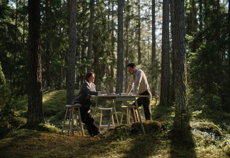a man and a woman are sitting at a table in the woods .