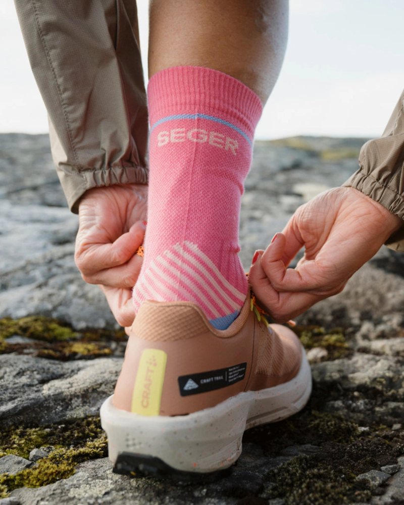 Person lacing up a beige trail running shoe, wearing pink socks with "SEGER" on them.