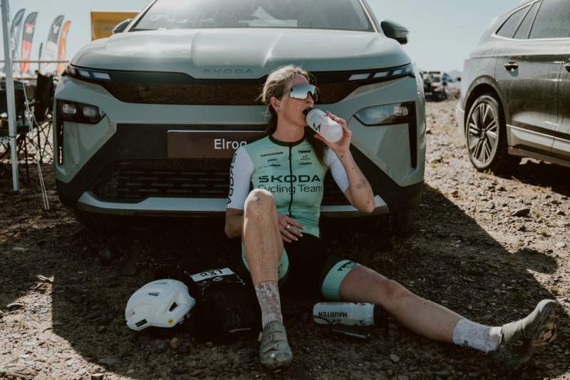 a woman is sitting on the ground drinking water in front of a car .