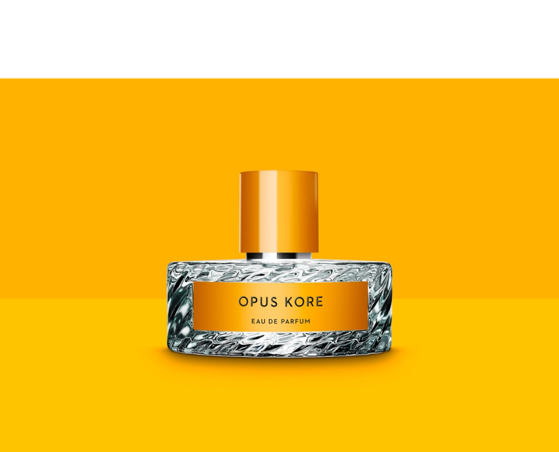 Opus Kore perfume bottle with a textured glass base, orange label, and orange cap, on an orange background.