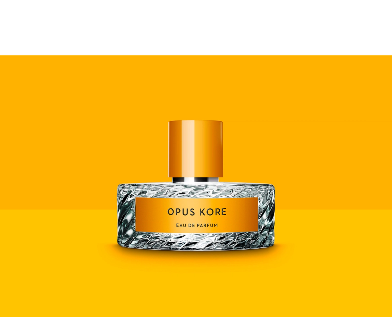 Opus Kore perfume bottle with a textured glass base, orange label, and orange cap, on an orange background.